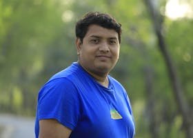 pexels-photo-11924965-11924965 A man in a blue shirt poses on a peaceful park road surrounded by green trees.